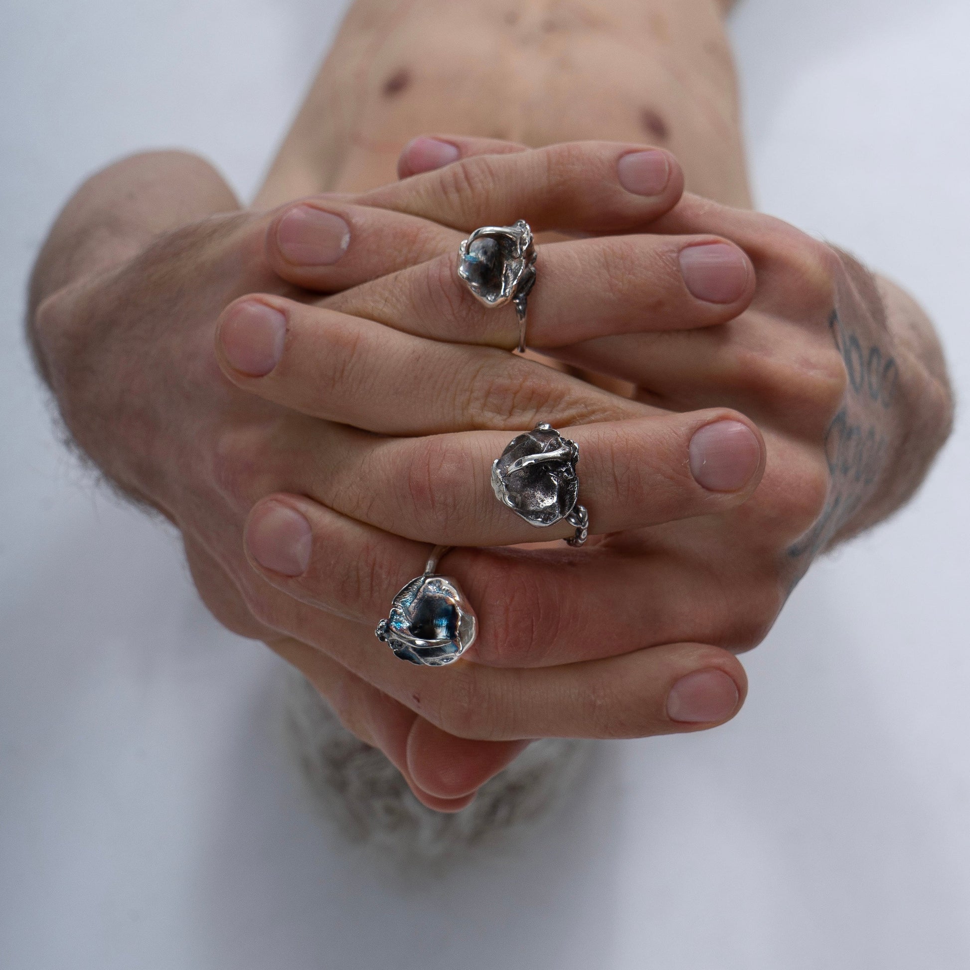 A model's hands adorned with multiple Rhinoceros Beetle Rings, showing the striking silver details from different angles. The composition emphasizes the sculptural quality of the jewelry against the model’s skin.