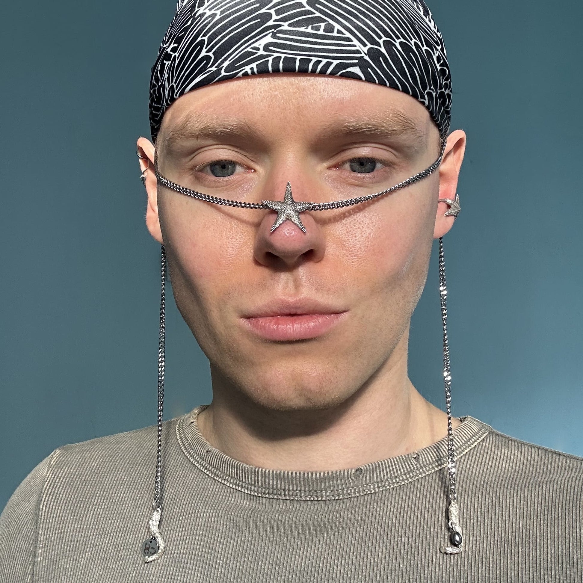 A model wearing the Starfish Facechain with a headscarf and neutral-toned outfit. The starfish-shaped centerpiece rests on the nose bridge, while the chains drape elegantly along the sides of the face.