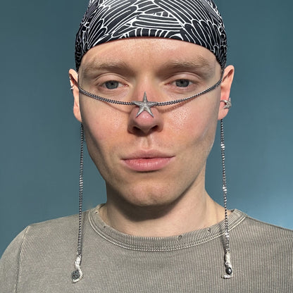A model wearing the Starfish Facechain with a headscarf and neutral-toned outfit. The starfish-shaped centerpiece rests on the nose bridge, while the chains drape elegantly along the sides of the face.